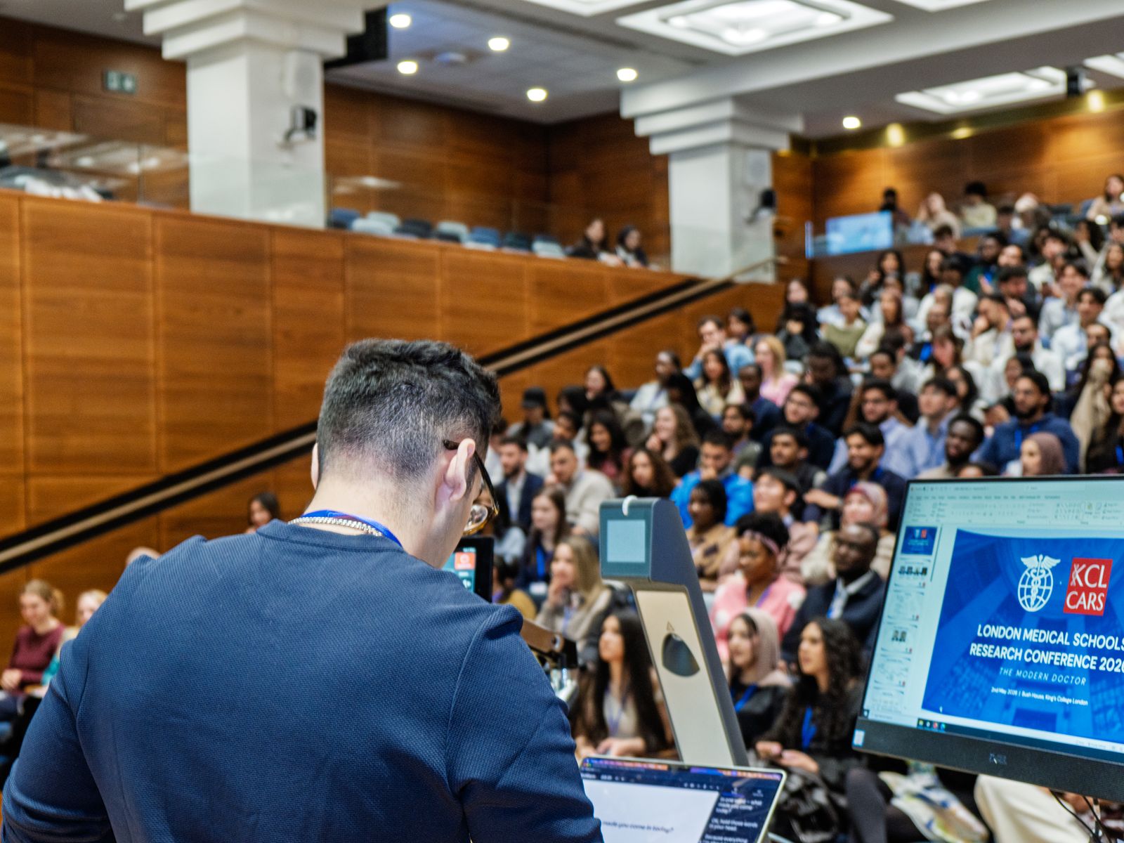A speaker addressing a packed auditorium, photographed by Kyros